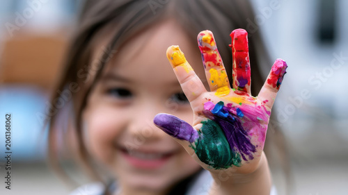 Happy little child showing colorful painted hand at camera, messy fingers covered in vibrant paint, enjoying creative art activity for early childhood education and development