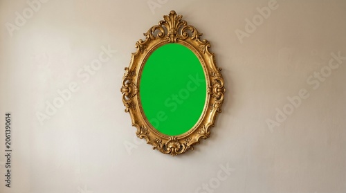 Golden ornate oval mirror with green screen on a beige wall, perfect for virtual backgrounds or creative editing