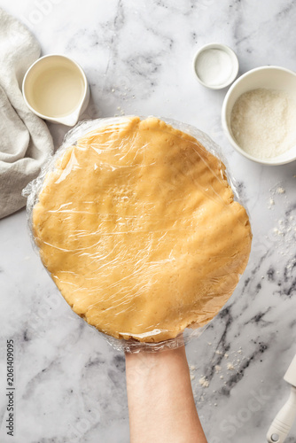 Process of making a base for shortbread pie, tart or quiche. Woman's hands hold the dough in cling film for subsequent cooling. Home baking culinary concept, recipe. Flat lay