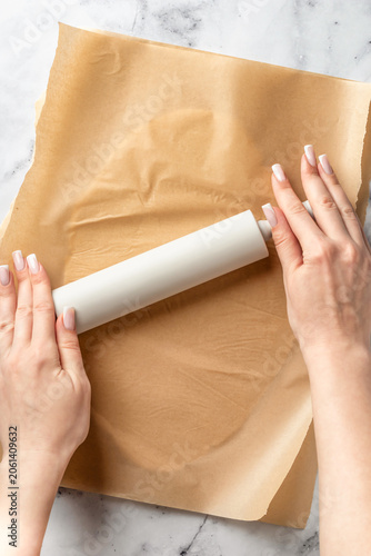 Process of making a base for shortbread pie, tart or quiche. Woman's hands roll out dough between sheets of parchment. Home baking culinary concept, recipe. Flat lay
