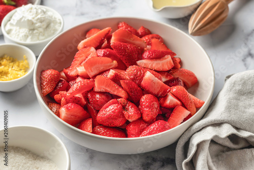 Process of making a strawberry pie tart filling. Fresh cutted berries in white bowl on marble background. Home baking culinary concept, recipe