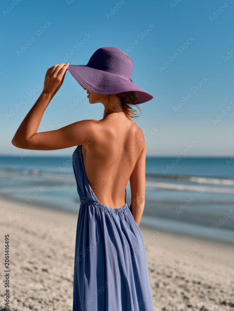 Fototapeta premium Woman backless dress purple hat beach sand ocean summer sunny day fashion style vacation