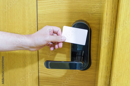 Hand using a key card to unlock a hotel room door, close-up of electronic access control system on a wooden door, representing travel, hospitality and modern security technology.