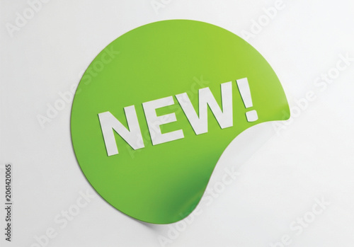 Bright green adhesive sticker with curled corner and white new text label isolated on plain light background concept for marketing promotion sales retail shop.
