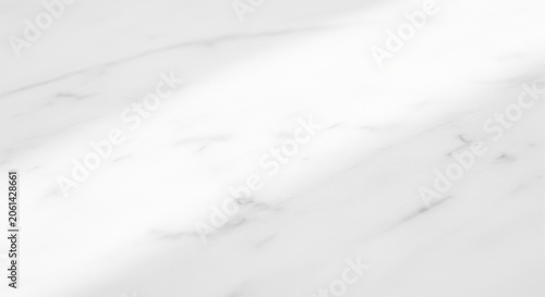 A bright, overexposed view looking across a smooth white marble surface with faint grey veins and a strong light glare coming from the top corner