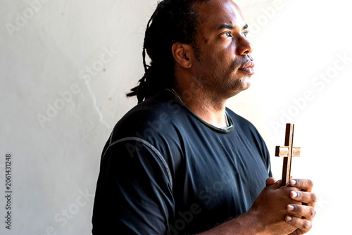 Fotografie Person holding a cross, gazing upward in contemplation.