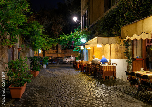 Night cozy old street with tables of restaurant in Trastevere in Rome, Italy. Trastevere is rione of Rome, on west bank of Tiber in Rome. Architecture and landmark of Rome