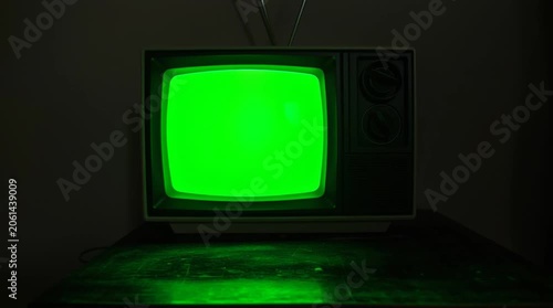 Vintage television with green screen turned on in a dark room during the evening