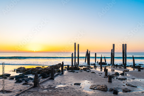 Historic petrified timber posts and stone foundation remains of the former Port Willunga jetty at sunset on the Fleurieu Peninsula, South Australia. 