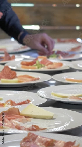 Vertical: A chef artfully plates an Italian appetizer combining thin slices of prosciutto, assorted cheese and fresh salad leaves, creating a colorful starter for guests at the celebration event.