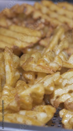 Vertical: A large tray filled with golden crispy french fries sits ready to be served, a simple crowd-pleasing side dish prepared for guests at the busy catered restaurant party event.