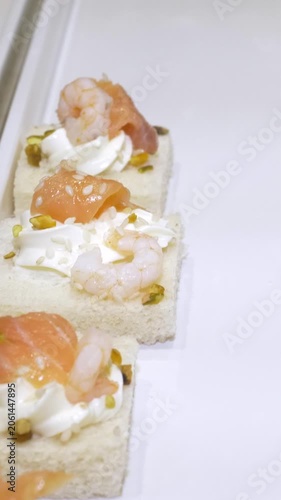 Vertical: Small canapés topped with fresh shrimp and creamy mayonnaise are carefully arranged on a serving tray, an elegant finger food prepared for guests at the catered party event.