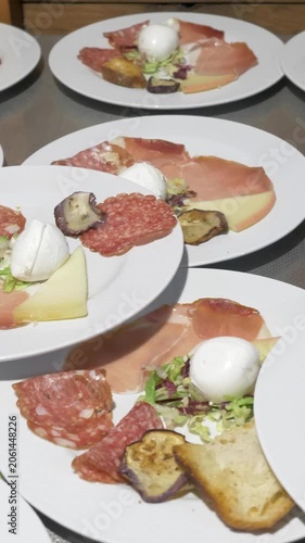 Vertical: A generous antipasto spread is ready for many guests, featuring mozzarella, grilled eggplant, prosciutto and more, showcasing the abundance prepared for the catered restaurant party event.
