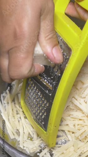 Vertical: Close-up of fresh parmesan cheese being grated by hand in the restaurant kitchen, releasing its rich aroma as it prepares to top a delicious pasta dish at the party event.