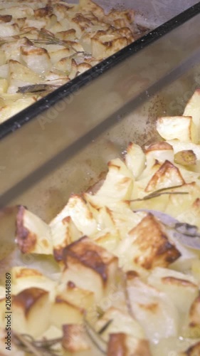 Vertical: A panoramic sweep reveals a tray filled with golden oven-baked potatoes, their crispy edges catching the light, a comforting side dish prepared for guests at the party event.