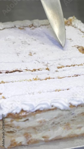 Vertical: A chef carefully slices through the celebration cake, preparing neat portions to be served as a sweet final course for guests enjoying the catered restaurant party event.