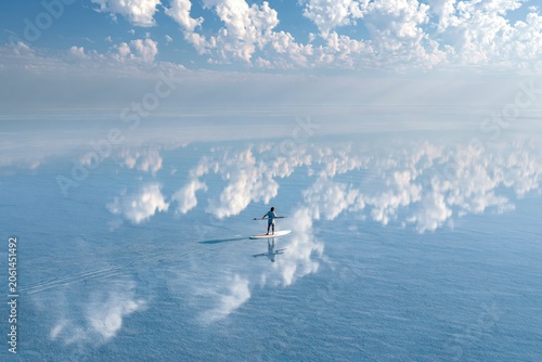 Healing scenery, breathtakingly beautiful. Vast blue sky with white clouds, boundless mirror-like water surface with a surfer