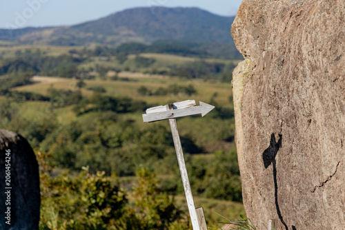 Directional Arrow Sign on Rocky Highland with Green Valley Landscape Behind