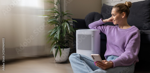 smiling woman sitting on the floor by air purifier in living room. air quality and microclimate control at home