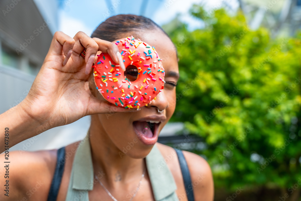 Fototapeta premium Young woman playfully holding pink donut over eye