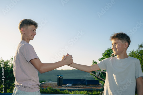 Obraz na plátně Two teenage boys shaking hands and looking at each other outdoors, concept of ag