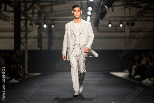 Male Asian model walking on a fashion runway wearing a stylish light grey linen suit at a catwalk show