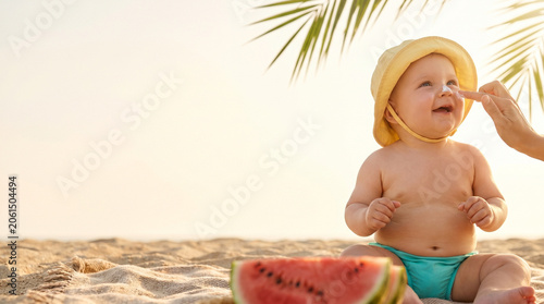 Baby enjoying summer day on beach with watermelon and palm tree  