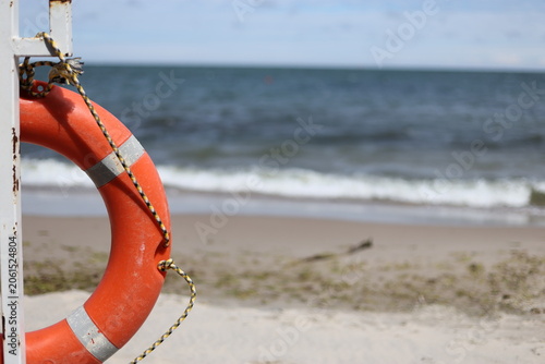 Принти на полотні Orange lifebuoy hanging on post at sandy beach near ocean
