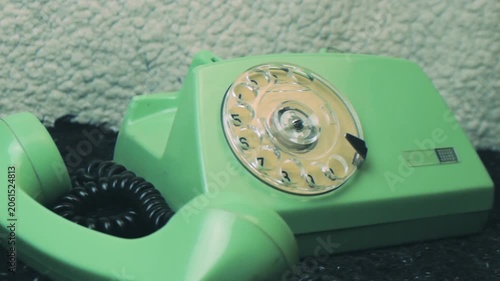 Close-up shot hand picking up receiver of a vintage green rotary telephone. The outdated piece of technology resting on textured surface. Communication method from the last century