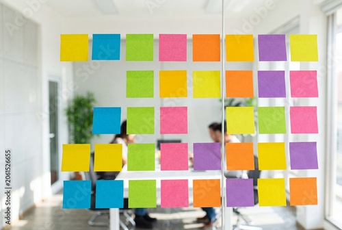 Professional business team brainstorming session inside a modern office with colorful sticky notes arranged on a glass wall during corporate meeting