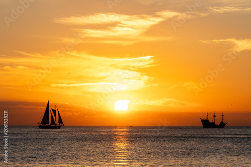 A sunset cruise and small sailboat silhouetted against the setting sun over a calm ocean. 