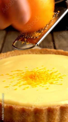 Hand using grater to shred ripe orange over cake