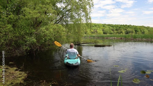 Middle-aged kayaker paddling away from the river shoreline