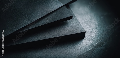Abstract Material Surface: Close-up, moody shot of stacked dark gray abstract material, with subtle texture and dramatic lighting creating depth and shadow.