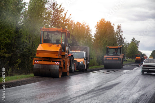 Fotografie Orange road rollers compacting new asphalt surface during daytime road construction operations