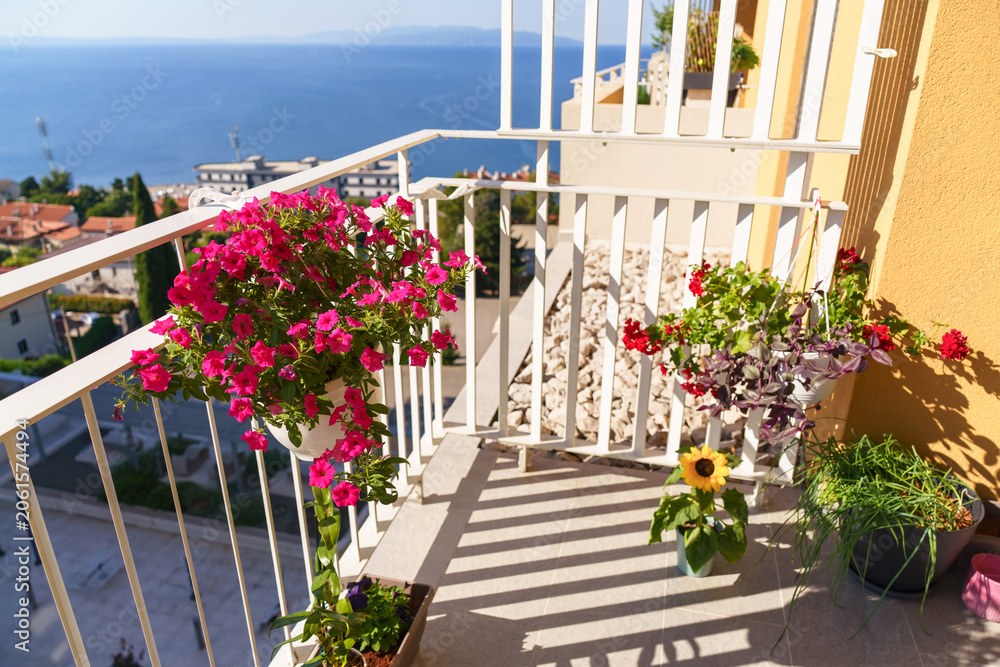 Obraz premium Colorful balcony garden with blooming flowers and stunning sea panorama on a sunny summer day. Concept of urban gardening, Mediterranean lifestyle and outdoor living