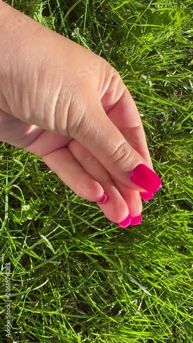 Close-up feemale hand with pink gel polished manicure on grass background, vertical video 