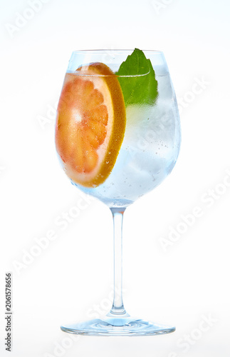 A refreshing summer cocktail with ice cubes, a fresh slice of pink grapefruit, and a green mint leaf in a glass, isolated on a clean white background.
