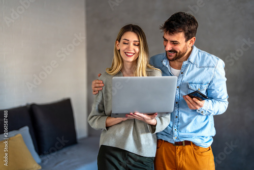 Happy young diverse, multiethnic couple planning budget, reading good news on laptop at home