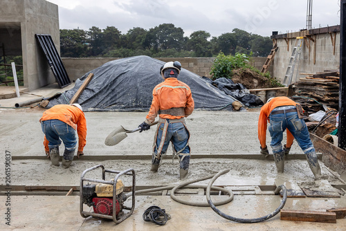 Construction crew using screed board and hand tools to level and finish freshly poured concrete slab during residential building construction