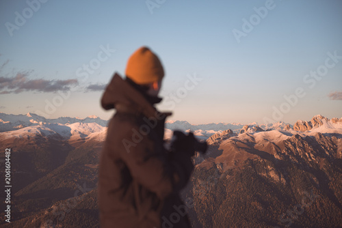 Photographer admiring snow-covered mountain ranges during sunset in the Dolomites. Atmospheric alpine landscape with warm evening light and distant peaks