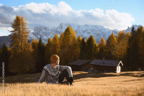 Canvas Print Person relaxing on an alpine meadow surrounded by golden larch trees in the Dolomites