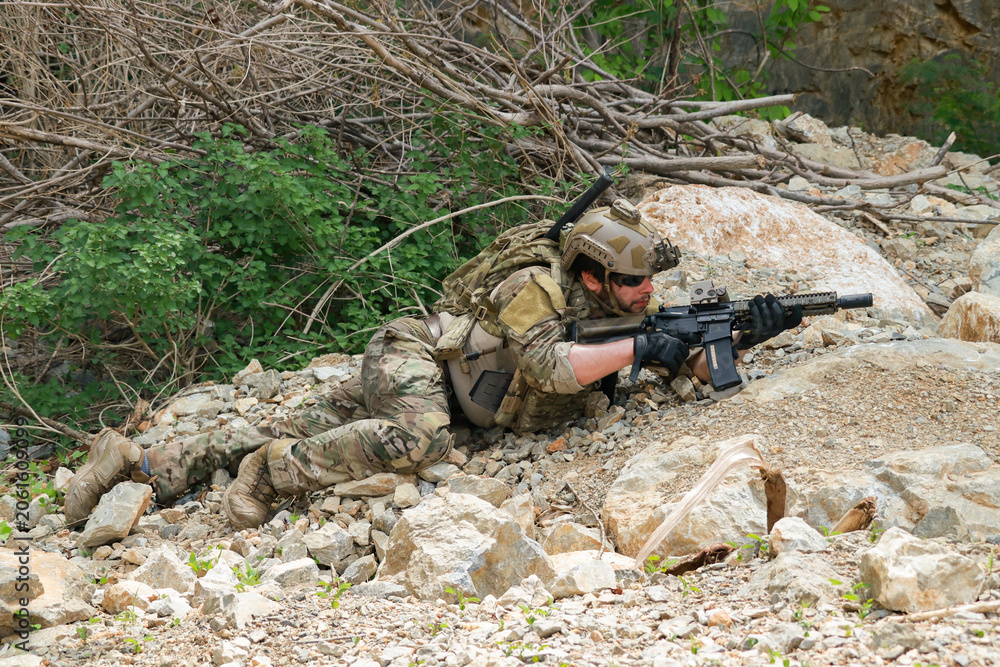 Fototapeta premium The sacrificing soldiers lie prostrate on the ground camouflaged behind rocks preparing fire upon the enemy on the ground in a ready to attack stance.