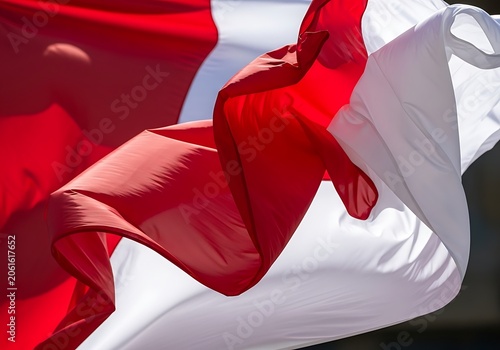 A vibrant red and white flag billows gracefully in the wind, showcasing dynamic folds and shadows under bright sunlight.