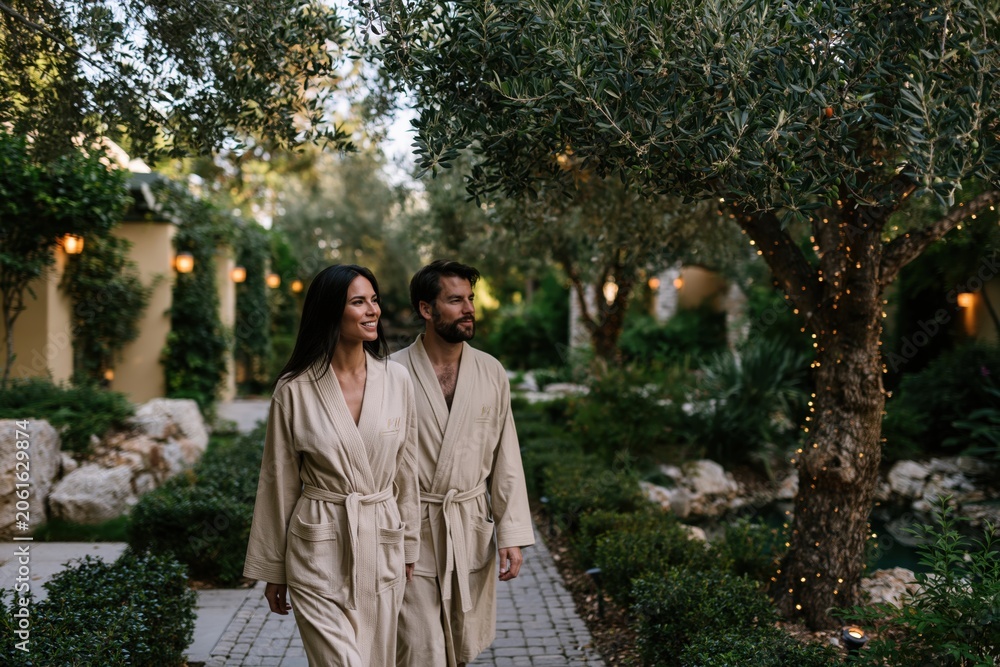 Fototapeta premium Couple walking in bathrobes at spa resort garden