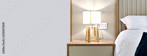 Stylish wooden bedside table and lamp illuminates cozy bedroom interior design. Comfortable home decor living concept, horizontal view background, copy space, no people