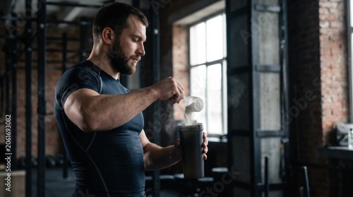 Athletic man pouring protein powder into shaker in gym