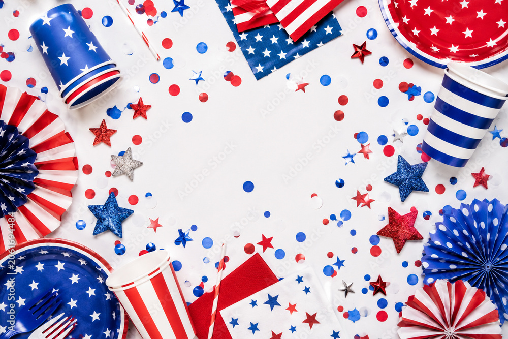 Obraz premium Fourth of July party supplies scattered on white surface with red blue white confetti.