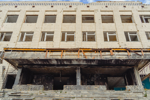 The facade of a destroyed public building with broken windows and a fire damaged porch entrance after recent military shelling and боевых действий