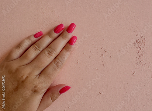 Close-up feemale hand with pink gel polished manicure on peach background,photo